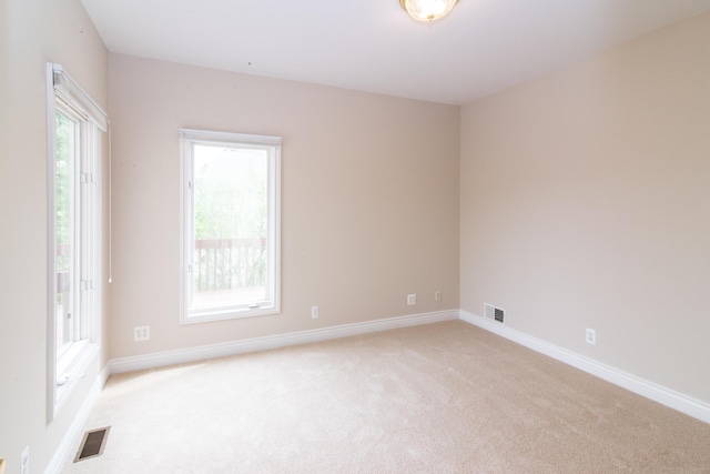 empty room featuring light colored carpet, visible vents, and baseboards