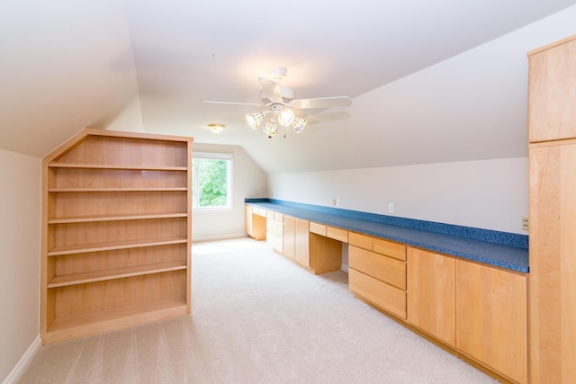 unfurnished office featuring lofted ceiling, a ceiling fan, built in study area, light carpet, and baseboards