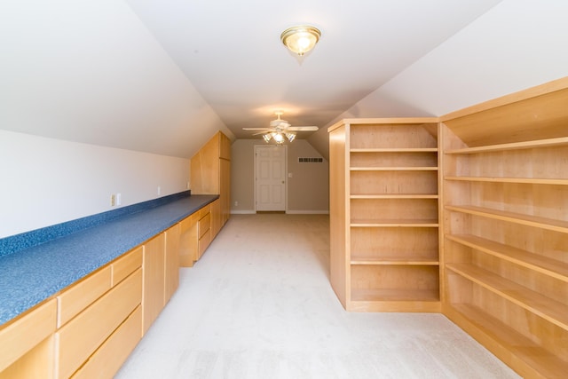 interior space featuring light colored carpet, visible vents, light brown cabinetry, vaulted ceiling, and ceiling fan