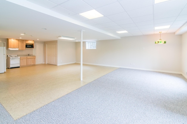 below grade area with freestanding refrigerator, a drop ceiling, and baseboards