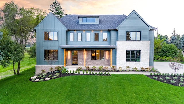 modern farmhouse featuring brick siding, roof with shingles, a porch, board and batten siding, and a front yard