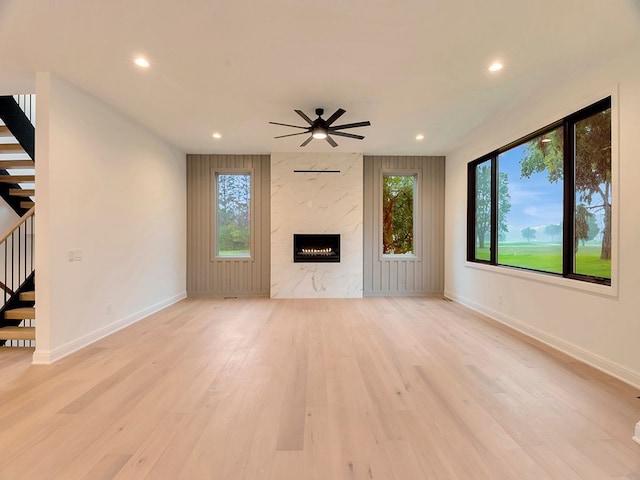 unfurnished living room with light wood-type flooring, stairway, a fireplace, and a wealth of natural light