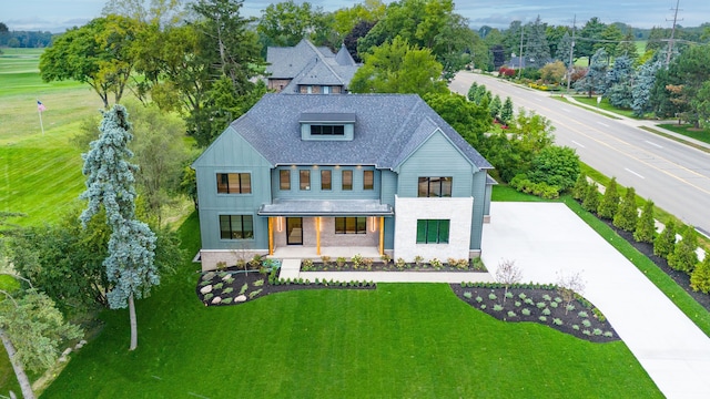 modern farmhouse featuring covered porch, a front lawn, concrete driveway, and roof with shingles