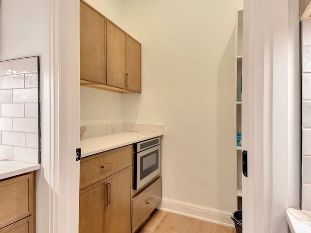 kitchen featuring light countertops, stainless steel microwave, light wood-style flooring, and baseboards