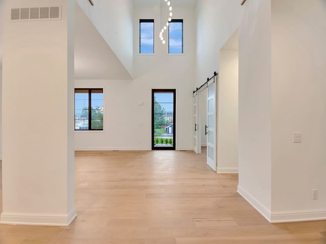 foyer featuring a barn door, visible vents, baseboards, a high ceiling, and light wood-style floors