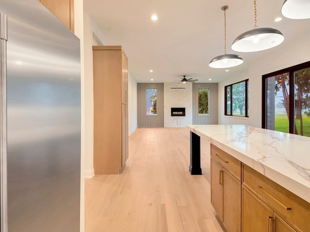 kitchen with light wood finished floors, a premium fireplace, light stone counters, stainless steel built in fridge, and recessed lighting