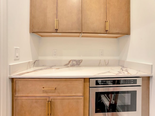 kitchen with oven, light brown cabinets, and light stone countertops