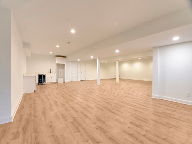 finished below grade area featuring baseboards, indoor bar, wine cooler, light wood-style floors, and recessed lighting