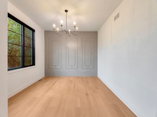 unfurnished dining area featuring baseboards, light wood-style floors, visible vents, and an inviting chandelier