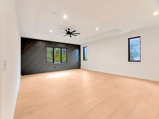 spare room featuring ceiling fan, a tray ceiling, light wood-type flooring, and baseboards