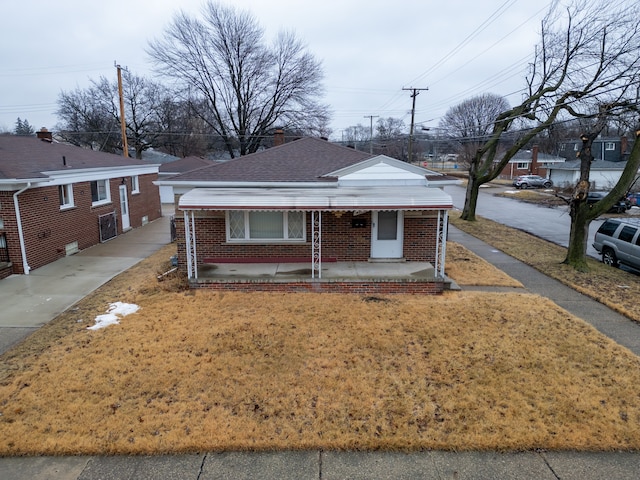 bungalow with covered porch, brick siding, a front lawn, and a shingled roof