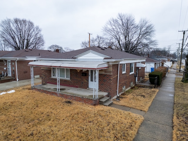 bungalow-style house featuring a shingled roof, a front lawn, and brick siding