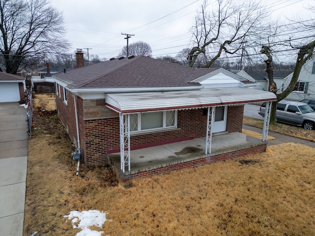 bungalow-style home with a patio area, brick siding, a chimney, and roof with shingles