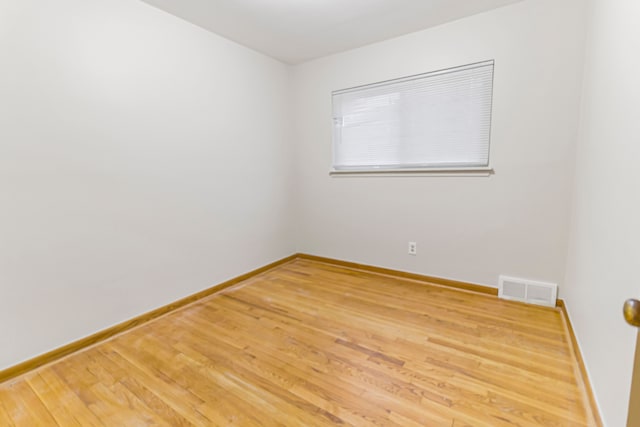 empty room with wood finished floors, visible vents, and baseboards