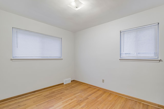 empty room with light wood-type flooring, visible vents, and baseboards