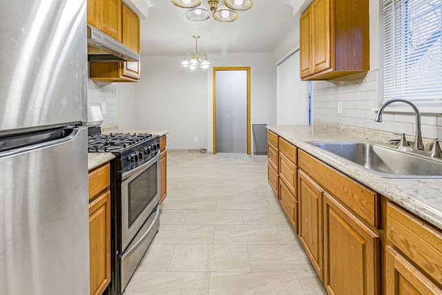 kitchen with an inviting chandelier, light countertops, stainless steel appliances, under cabinet range hood, and a sink