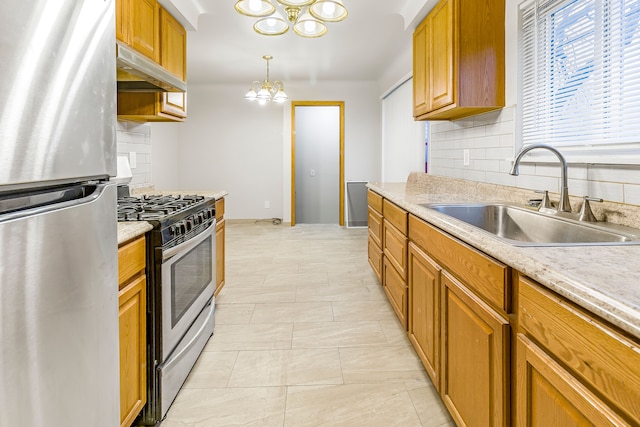 kitchen featuring appliances with stainless steel finishes, light countertops, under cabinet range hood, a chandelier, and a sink