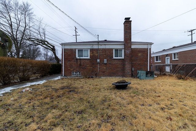 rear view of house with brick siding, a chimney, a lawn, fence, and a fire pit