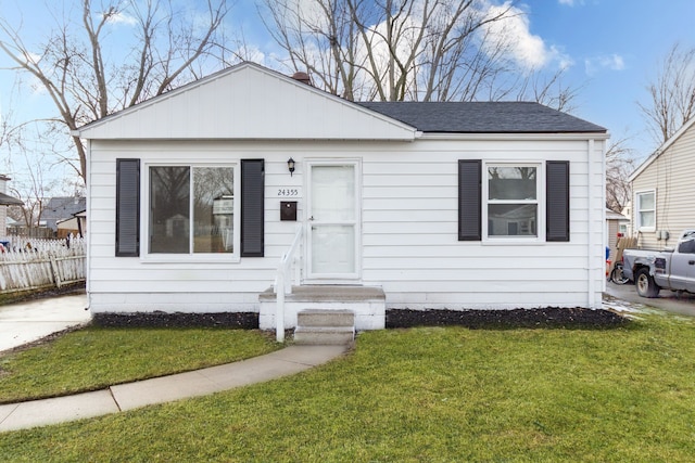 bungalow with a shingled roof, a front yard, and fence