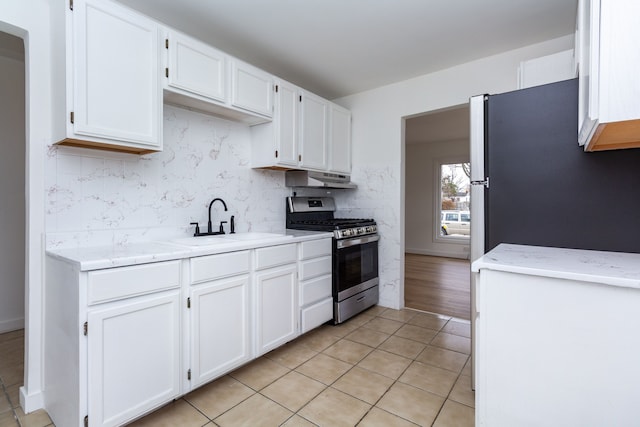 kitchen featuring under cabinet range hood, stainless steel gas range oven, white cabinets, and a sink