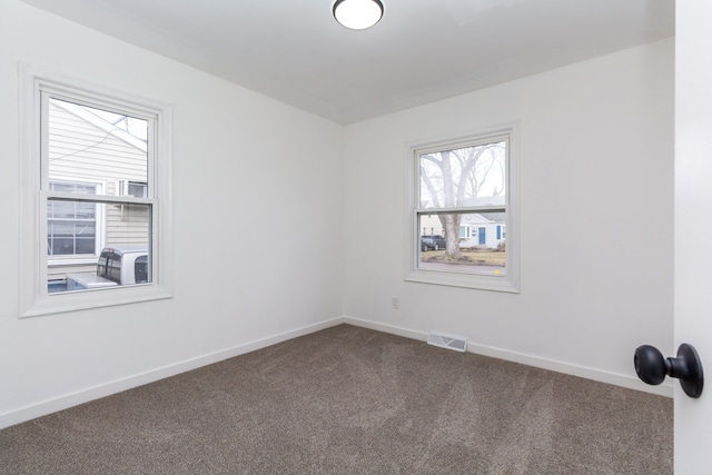 unfurnished room with baseboards, visible vents, and dark colored carpet