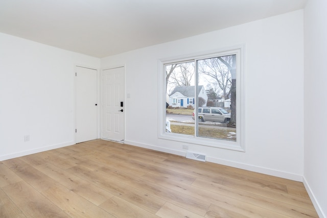 empty room with light wood-type flooring, visible vents, and baseboards