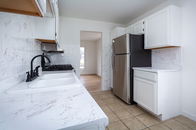 kitchen with light tile patterned flooring, a sink, white cabinetry, light countertops, and freestanding refrigerator