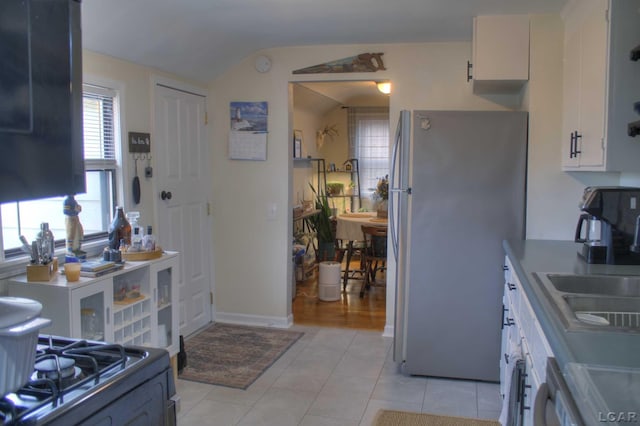 kitchen with freestanding refrigerator, gas stove, white cabinets, a sink, and light tile patterned flooring