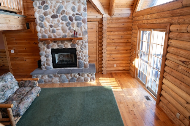 unfurnished living room featuring hardwood / wood-style floors, a stone fireplace, log walls, and visible vents