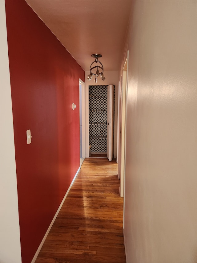 corridor with a notable chandelier, baseboards, and wood finished floors