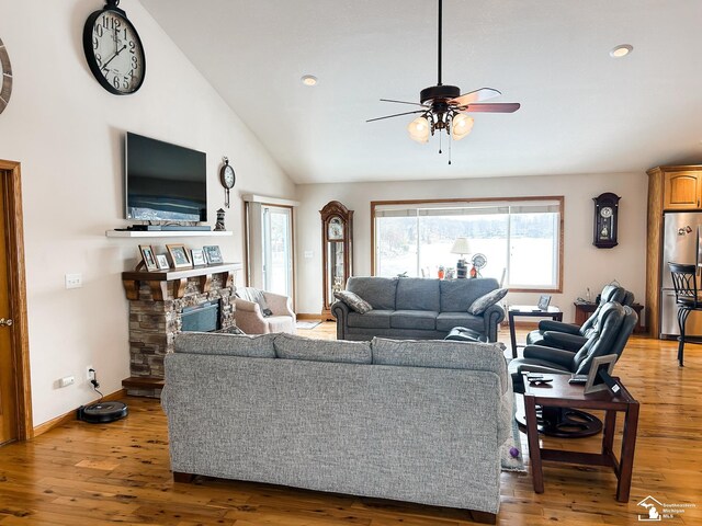 living room featuring light wood-type flooring, baseboards, lofted ceiling, and a stone fireplace