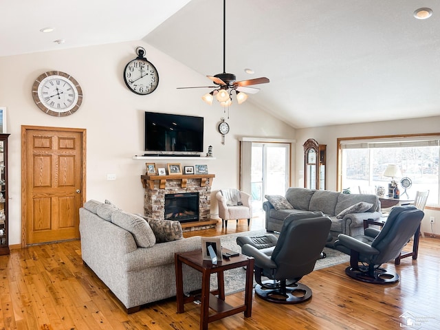 living area with a stone fireplace, light wood finished floors, high vaulted ceiling, and a ceiling fan