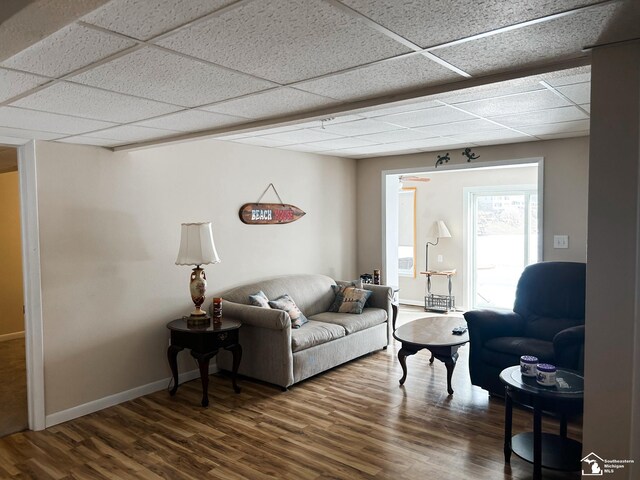 living room featuring a paneled ceiling, baseboards, and wood finished floors