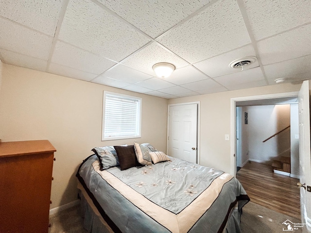 bedroom with baseboards, visible vents, a drop ceiling, and wood finished floors