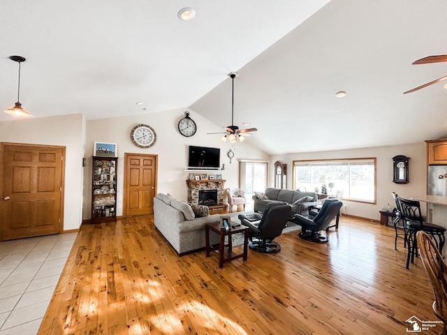 living room with high vaulted ceiling, a stone fireplace, a ceiling fan, baseboards, and light wood-type flooring