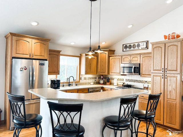 kitchen featuring lofted ceiling, a breakfast bar, a sink, light countertops, and appliances with stainless steel finishes