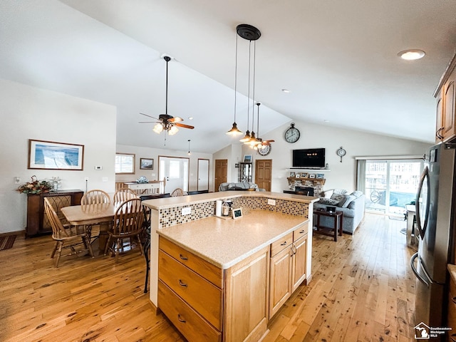 kitchen featuring freestanding refrigerator, open floor plan, vaulted ceiling, a stone fireplace, and light wood-type flooring