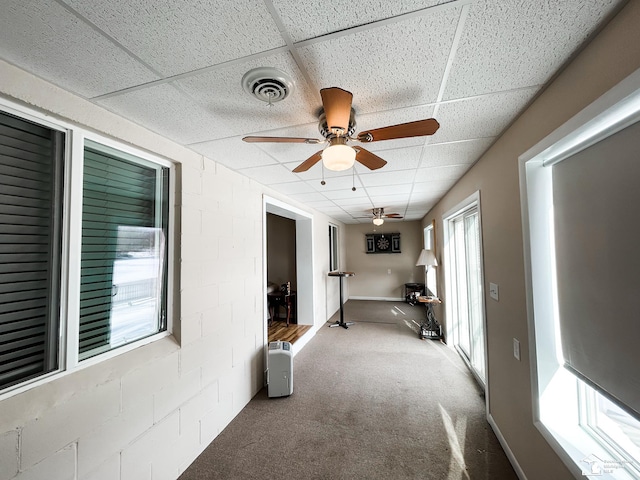 corridor with a drop ceiling, carpet flooring, a sunroom, visible vents, and concrete block wall