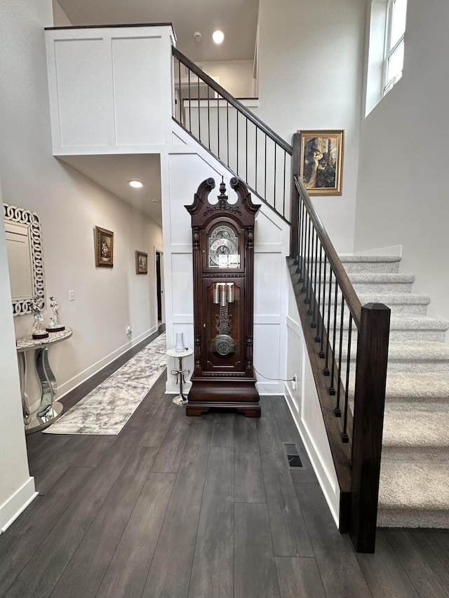 entrance foyer with a high ceiling, visible vents, baseboards, stairway, and dark wood finished floors