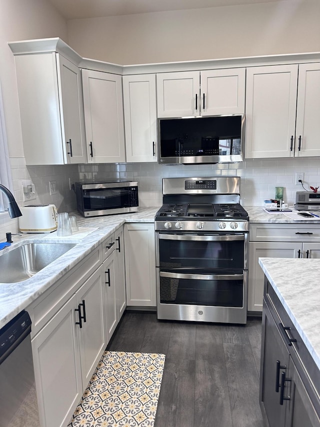 kitchen featuring white cabinets, dark wood-style flooring, a sink, stainless steel appliances, and backsplash