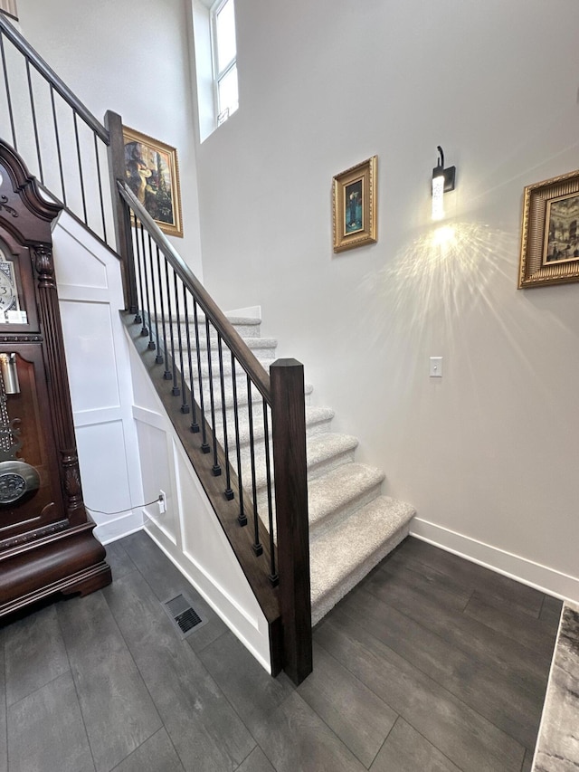 staircase featuring a high ceiling, baseboards, and wood finished floors