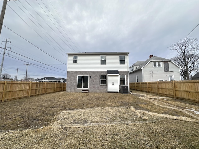 back of property with brick siding, central AC unit, and a fenced backyard