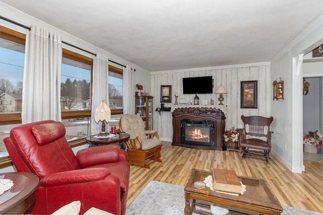 living area with ornamental molding, a glass covered fireplace, baseboards, and wood finished floors