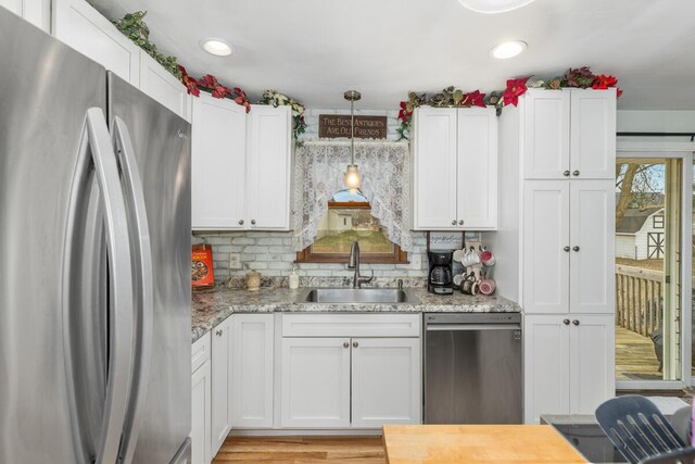 kitchen with tasteful backsplash, white cabinets, appliances with stainless steel finishes, hanging light fixtures, and a sink