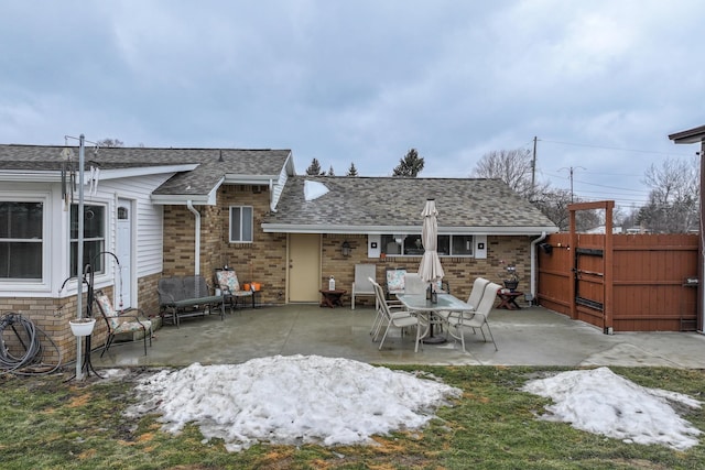 back of house with brick siding, roof with shingles, fence, and a patio