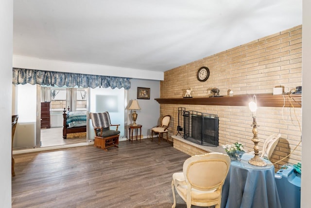 living area with a brick fireplace, brick wall, and wood finished floors