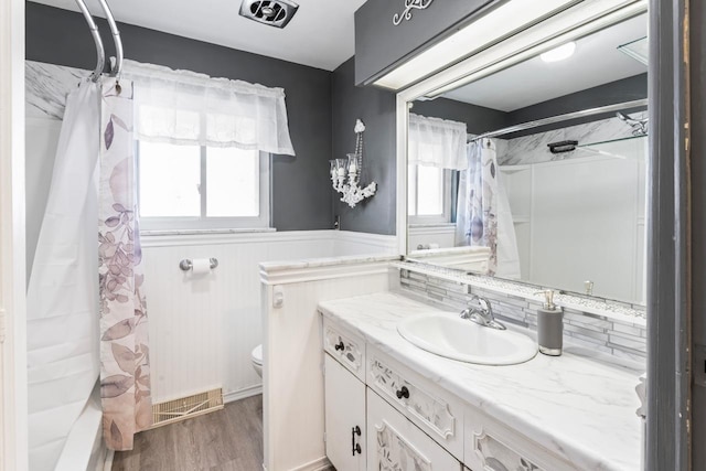 bathroom with toilet, a wainscoted wall, visible vents, and wood finished floors