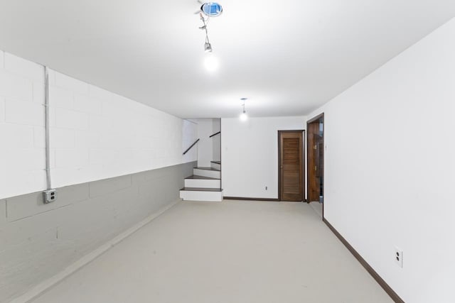 below grade area with stairway, concrete block wall, and baseboards