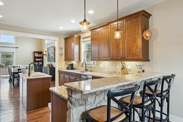 kitchen featuring a center island with sink, dark wood-style flooring, a peninsula, light stone countertops, and a sink