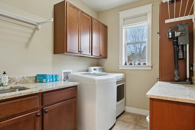 laundry room with cabinet space, light tile patterned floors, baseboards, washing machine and clothes dryer, and a sink